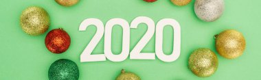 Beyaz 2020 rakamlarının üst görüntüsü, yeşil arka planda çok renkli Noel mücevherleri, panoramik çekim