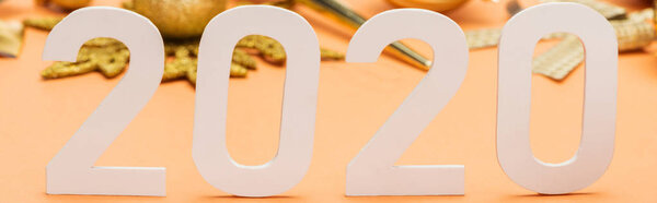 selective focus of white 2020 numbers in front of golden christmas decoration on orange background, panoramic shot