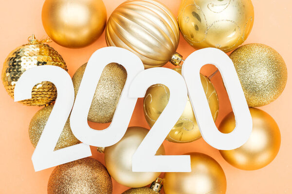 top view of white 2020 numbers on golden christmas balls on orange background