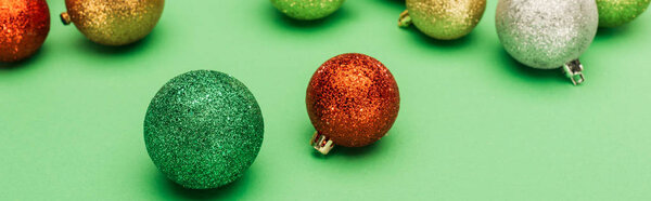 panoramic shot of multicolored Christmas baubles on green background