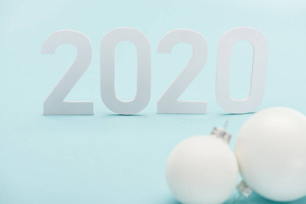 selective focus of white 2020 numbers near Christmas baubles on light blue background