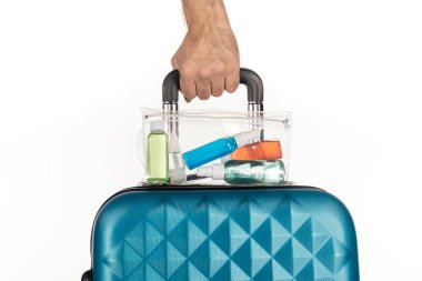 Beyaz arka planda renkli şişelerle dolu kozmetik çantalı seyahat çantası tutan adamın kırpılmış görüntüsü. 