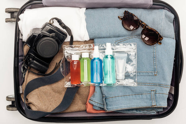 top view of travel bag with towel, cosmetic bag with colorful bottles, digital camera, clothes and sunglasses