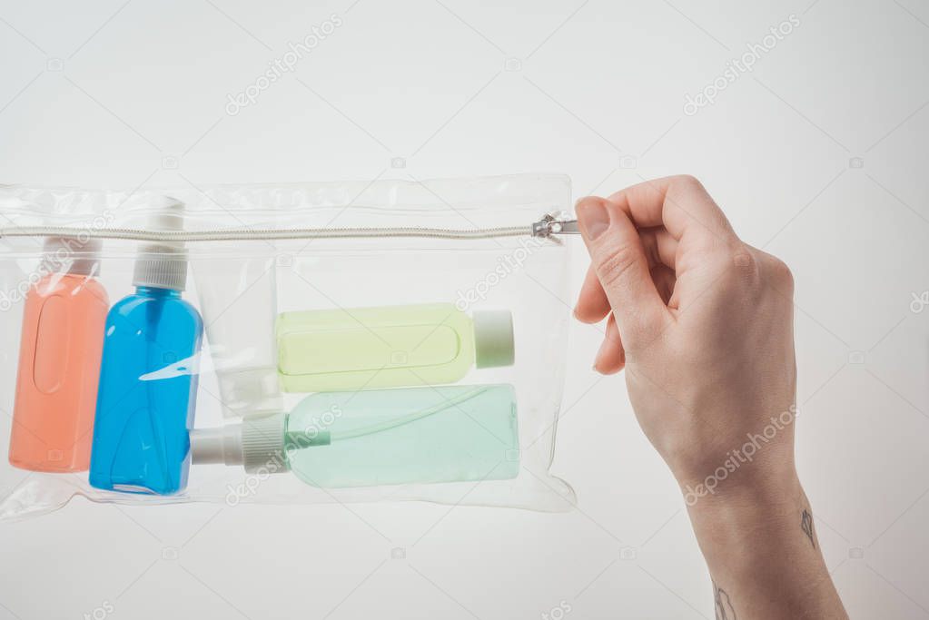 cropped view of woman holding cosmetic bag with colorful bottles with liquids on white background 