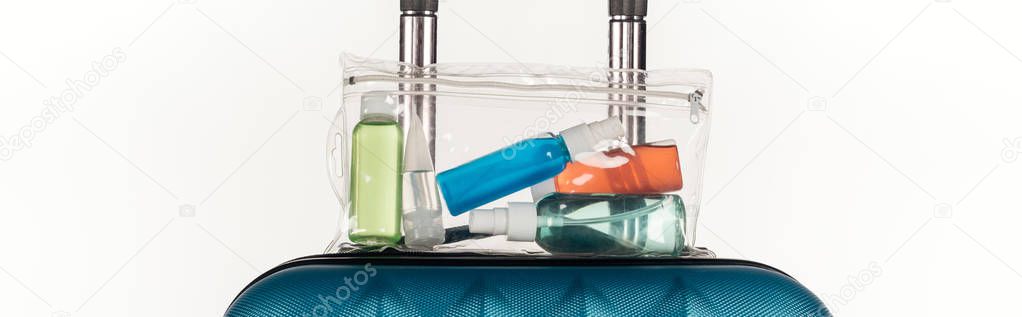 panoramic shot of travel bag with cosmetic bag with colorful bottles with liquids isolated on white
