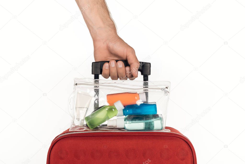 cropped view of man holding travel bag with cosmetic bag with colorful bottles with liquids on white background 