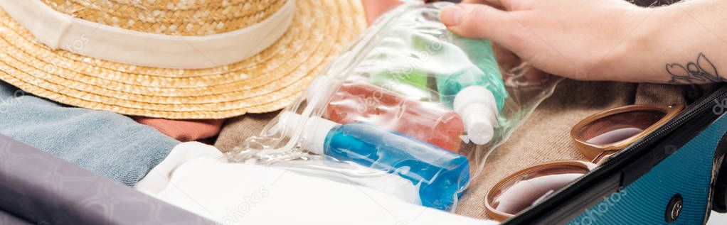 panoramic shot of woman packing travel bag with cosmetic bag with bottles
