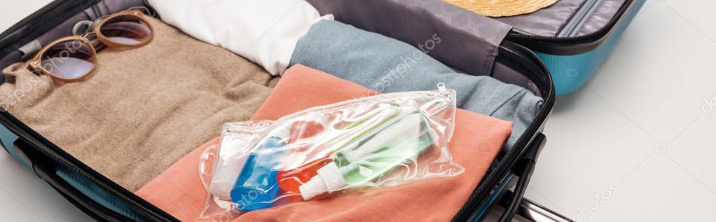 panoramic shot of travel bag with towel, cosmetic bag with bottles, clothes, sunglasses 