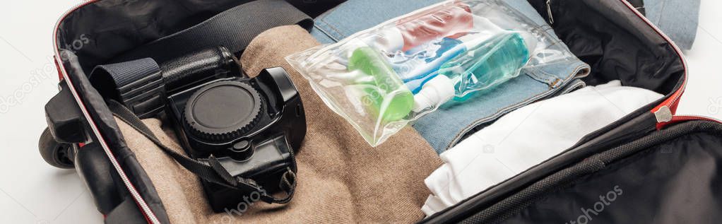 panoramic shot of travel bag with towel, cosmetic bag with colorful bottles, digital camera, clothes 
