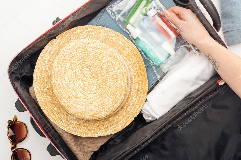 cropped view of woman packing travel bag with cosmetic bag with colorful bottles
