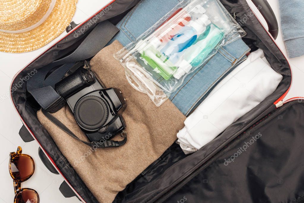 top view of travel bag with towel, cosmetic bag with colorful bottles, digital camera, clothes 