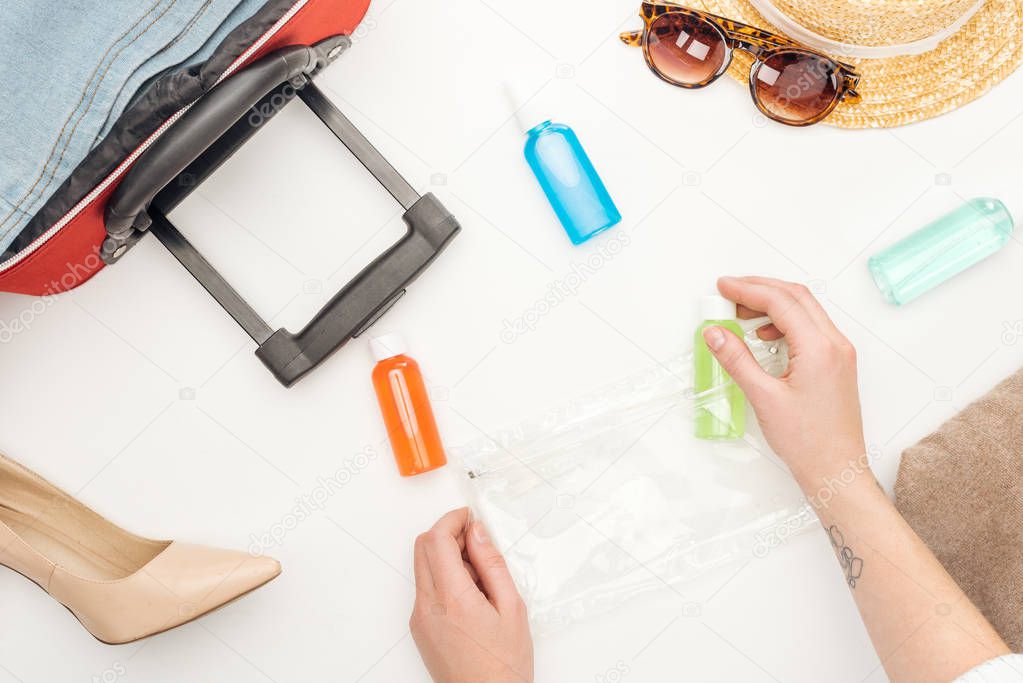 cropped view of woman holding cosmetic bag with colorful bottles on white background tattooed 