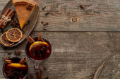 Draufsicht auf Kuchenstück und rot gewürzten Glühwein mit Beeren, Anis, Orangenscheiben und Zimt auf rustikalem Holztisch