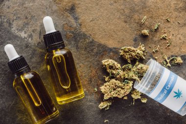 Tıbbi marihuana tomurcuklarının konteynır ve mermer yüzeyinde kenevir yağı bulunan şişelerin üst görüntüsü
