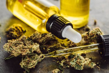 Tıbbi marihuana tomurcuklarını, şişe ve damlatıcıyı taş yüzeyinde kenevir yağıyla kapatın.
