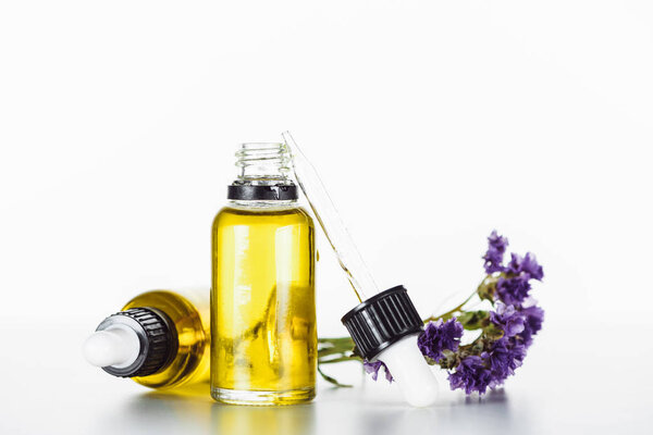 bottles of natural oil and twig of dry limonium with flowers isolated on white