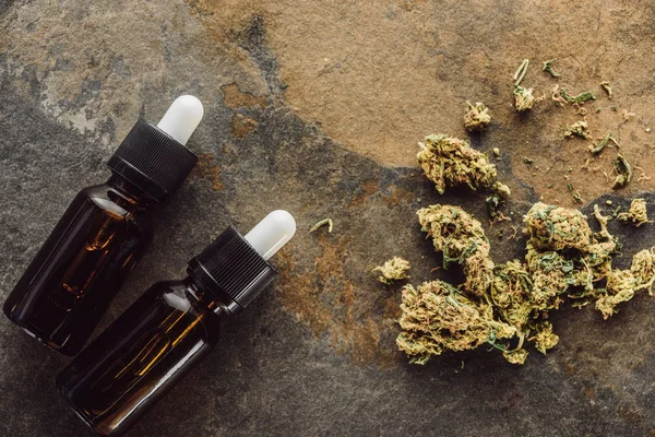 Mermer yüzeyinde kenevir yağı bulunan şişelerin yanındaki tıbbi marihuana tomurcuklarının üst görüntüsü