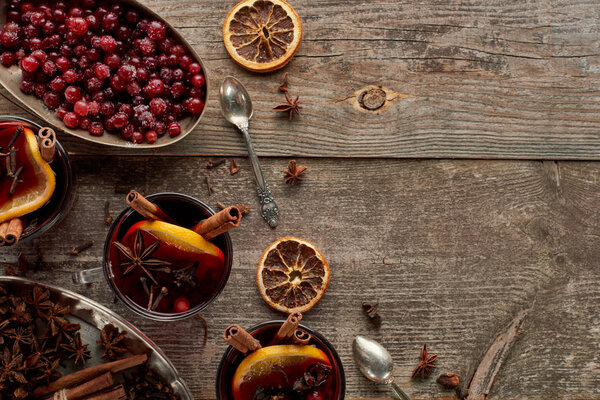 top view of red spiced mulled wine with berries, anise, orange slices and cinnamon on wooden rustic table
