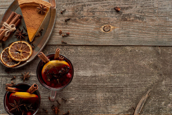 top view of piece of pie and red spiced mulled wine with berries, anise, orange slices and cinnamon on wooden rustic table