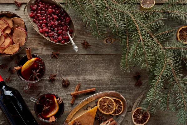 モミの枝 ベリー アニス オレンジのスライスと木の素朴なテーブルの上にシナモンの近くの赤いスパイスのマルチワインのトップビュー — ストック写真
