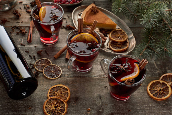 red spiced mulled wine near fir branch, pie, berries, anise, orange slices and cinnamon on wooden rustic table