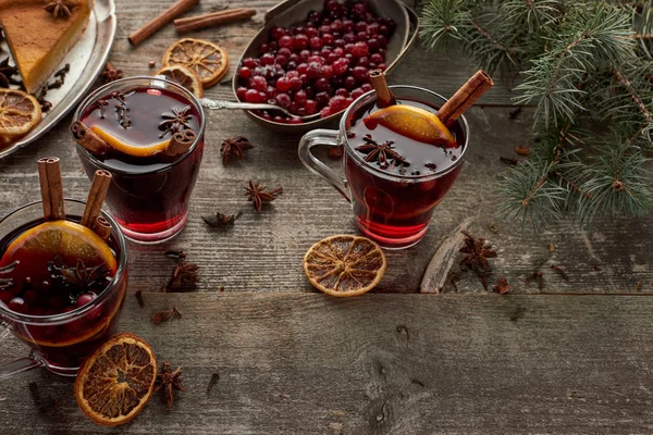 red spiced mulled wine near fir branch, berries, anise, orange slices and cinnamon on wooden rustic table