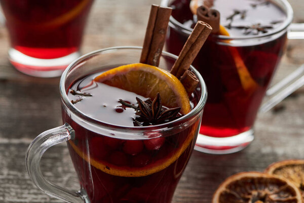 close up view of red spiced mulled wine with berries, anise, orange slice and cinnamon on wooden rustic table