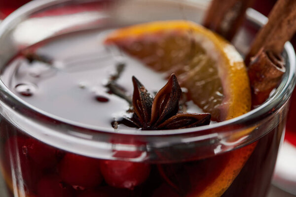 close up view of red spiced mulled wine with berries, anise, orange slice and cinnamon