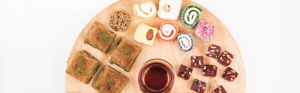 top view of wooden board with delicious turkish sweets and tea isolated on white, panoramic shot