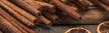 cinnamon sticks near dried citrus slices on wooden background, panoramic shot clipart