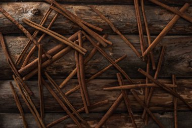 top view of cinnamon sticks scattered on wooden background clipart