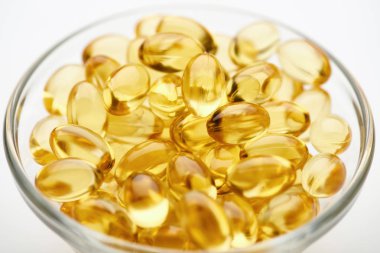 close up view of golden fish oil capsules in glass bowl on white background clipart