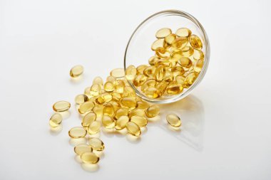golden fish oil capsules in glass bowl on white background clipart