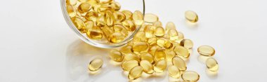 golden fish oil capsules in glass bowl on white background, panoramic shot clipart
