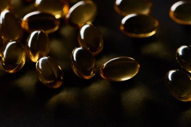 close up view of golden fish oil capsules on black background in dark clipart
