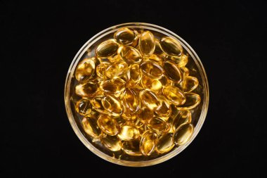 top view of golden fish oil capsules in glass bowl isolated on black clipart