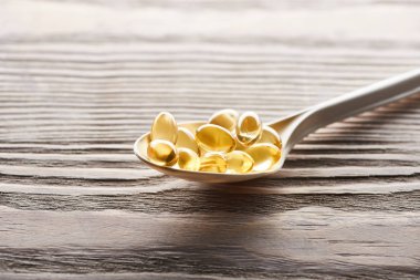 golden fish oil capsules in spoon on wooden table clipart