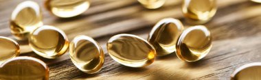 close up view of golden fish oil capsules scattered on wooden table, panoramic shot clipart