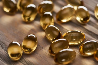 close up view of shiny golden fish oil capsules scattered on wooden table clipart