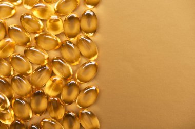 top view of golden shiny fish oil capsules on yellow background with copy space clipart