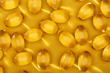 top view of golden shiny fish oil capsules scattered on yellow bright background clipart