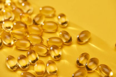 close up view of golden shiny fish oil capsules scattered on yellow bright background clipart
