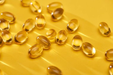 close up view of golden shiny fish oil capsules scattered on yellow bright background clipart