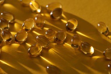 close up view of golden shiny fish oil capsules scattered on yellow background in dark clipart