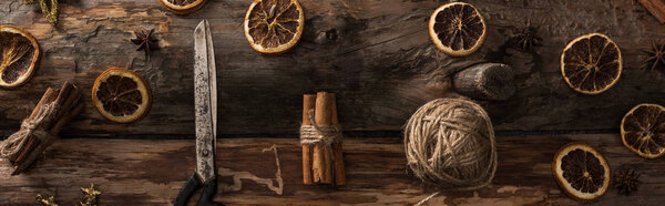 flat lay with cinnamon sticks, scissors, ball of thread on wooden background with winter decor, panoramic shot