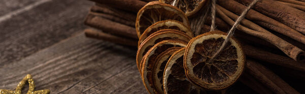 dried orange slices on thread and cinnamon on wooden background, panoramic shot