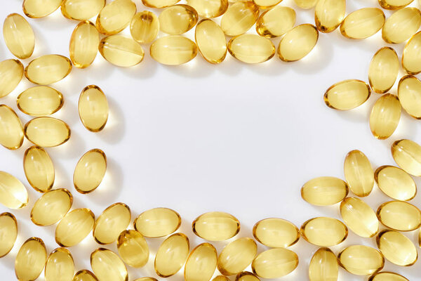 top view of golden fish oil capsules arranged in frame on white background