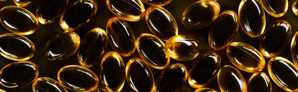 top view of golden fish oil capsules on black background in dark, panoramic shot