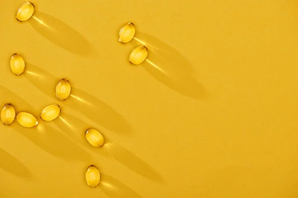 金光闪闪的鱼油胶囊分散在黄色明亮的背景上 有复制空间的顶部视图 — 图库照片