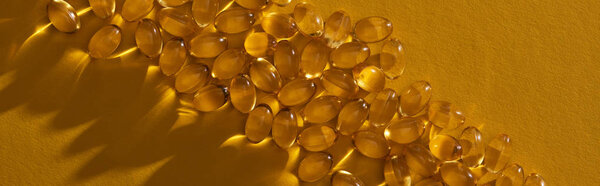 top view of golden shiny fish oil capsules on yellow background in dark, panoramic shot